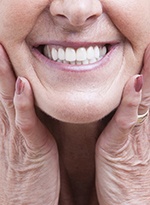 An up-close image of an older woman holding her face between her hands after receiving her customized dentures in Norwood