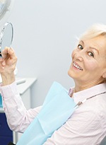 An older woman holding a handheld mirror at the dentist’s office and smiling