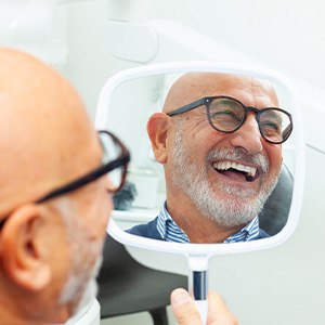 Older man smiling in the mirror at the dentist’s office