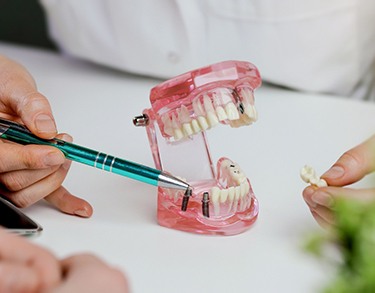 Dentist pointing to sample dental implant with pen while holding dental bridge in other hand