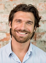 Bearded man smiling in front of a brick wall
