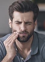 Young man grimacing and holding cheek