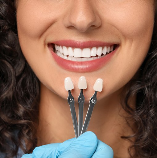 Nose-to-neck closeup of woman smiling with shade-guide held to teeth