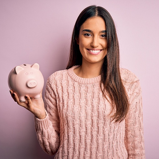 Smiling woman in pink sweater holding piggy bank with pink background