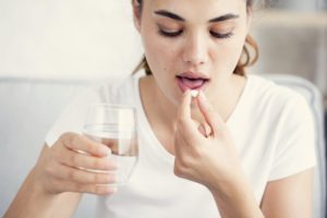 girl in white shirt taking a pill with water